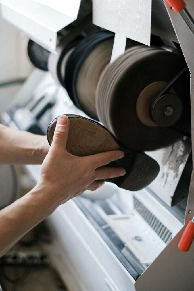 Detailed view of hands sanding a shoe sole in an industrial workshop. Perfect for illustrating craftsmanship.